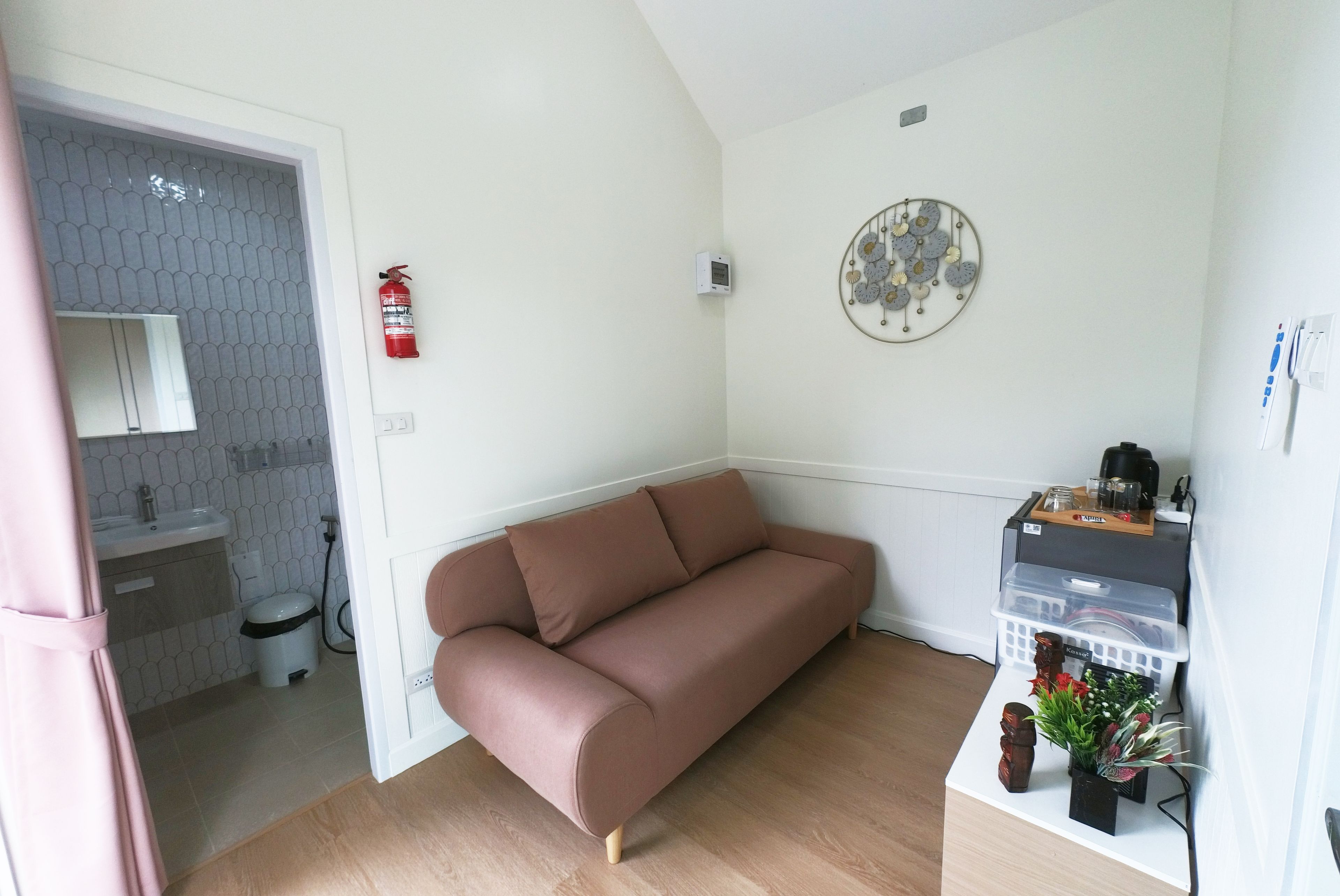 A compact living space with a sofa, a small kitchenette, a fire extinguisher, and a decorative wall piece.