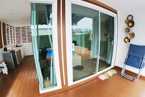 A room with a sliding glass door leading to an outdoor area, a small kitchenette, a blue chair, and a blue folding chair with slippers.