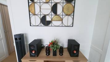 A room with a wooden console table, two black speakers, a decorative wall piece, and a tall black air purifier.