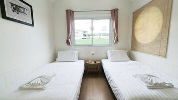 Habitación de hotel con dos camas individuales, una ventana con cortinas, una mesita de noche pequeña con lámpara y un cuadro en la pared.