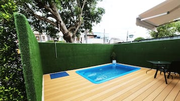 Una terraza de madera con piscina, rodeada de césped artificial verde y un árbol.