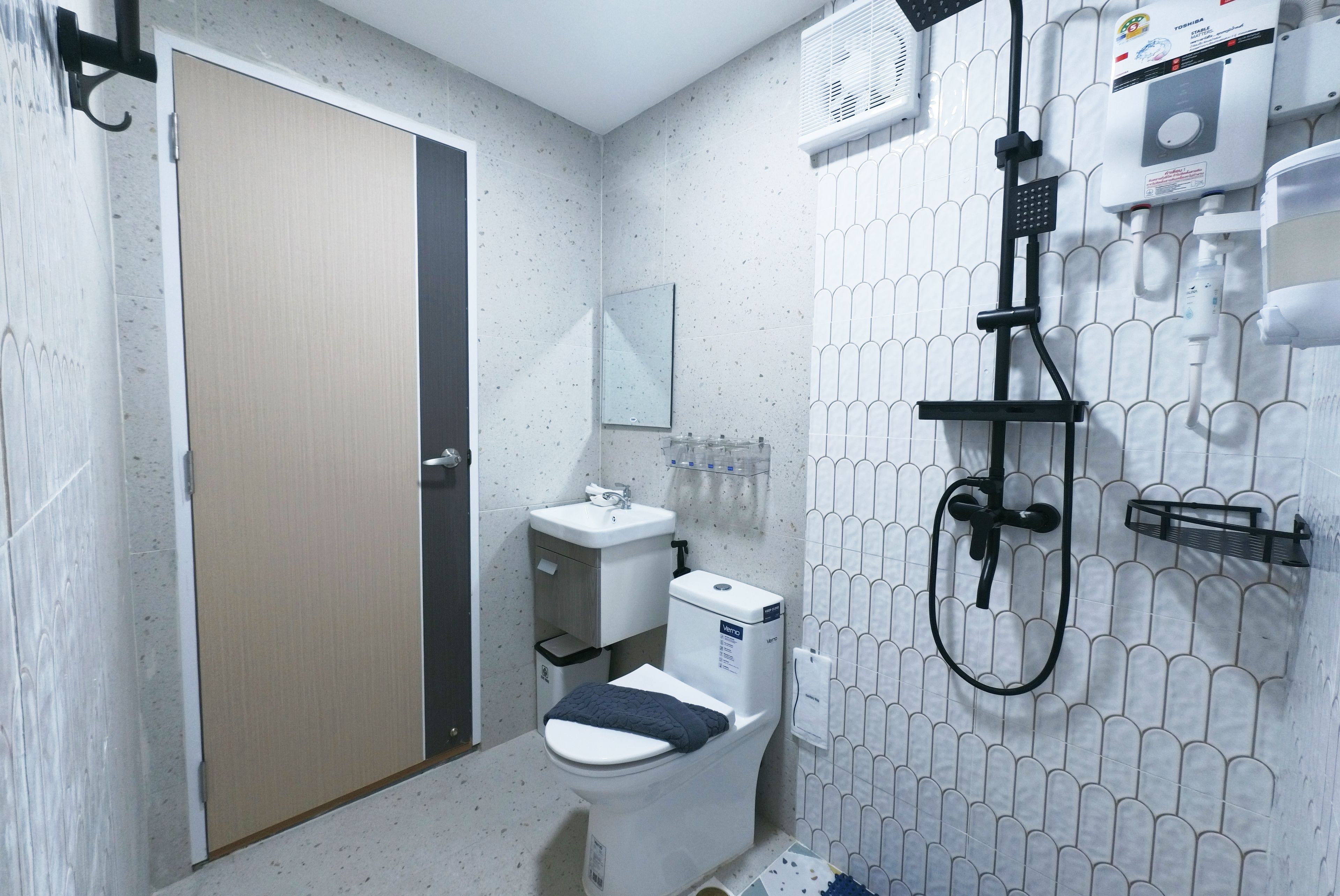 A bathroom with a toilet, sink, mirror, and a shower unit.