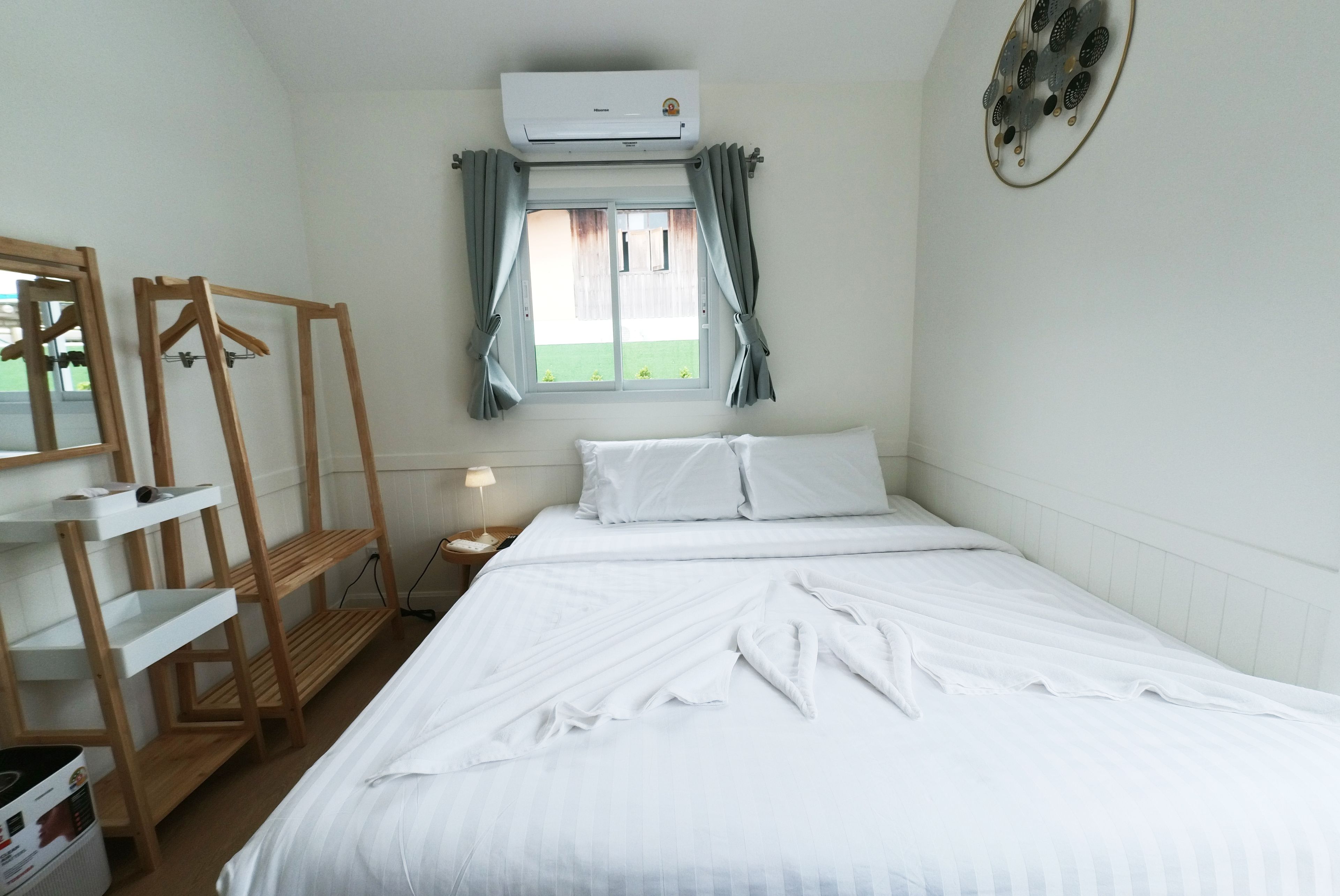 Habitación de hotel con cama, estantería de madera, espejo, equipo de aire acondicionado y ventana con cortinas.