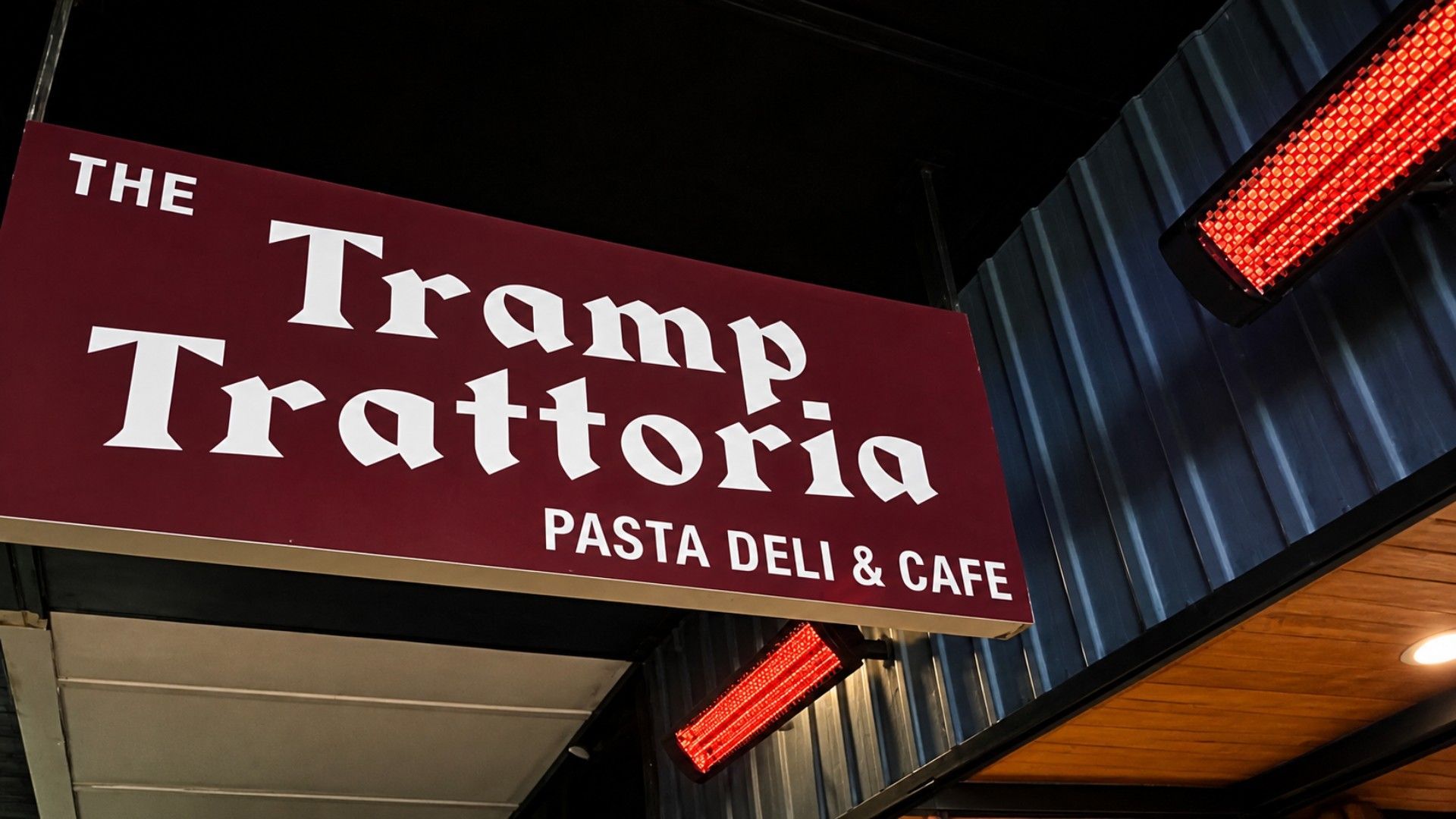 Une enseigne pour « The Tramp Trattoria Pasta Deli & Cafe », avec un fond bordeaux et des lettres blanches.