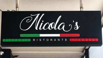 A sign with 'Nicola's' in cursive, indicating a pizzeria and restaurant, with a green and red bar suggesting Italian licensing.