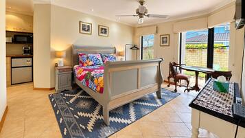 A bedroom with a bed, a desk, a chair, a window, and a kitchenette.