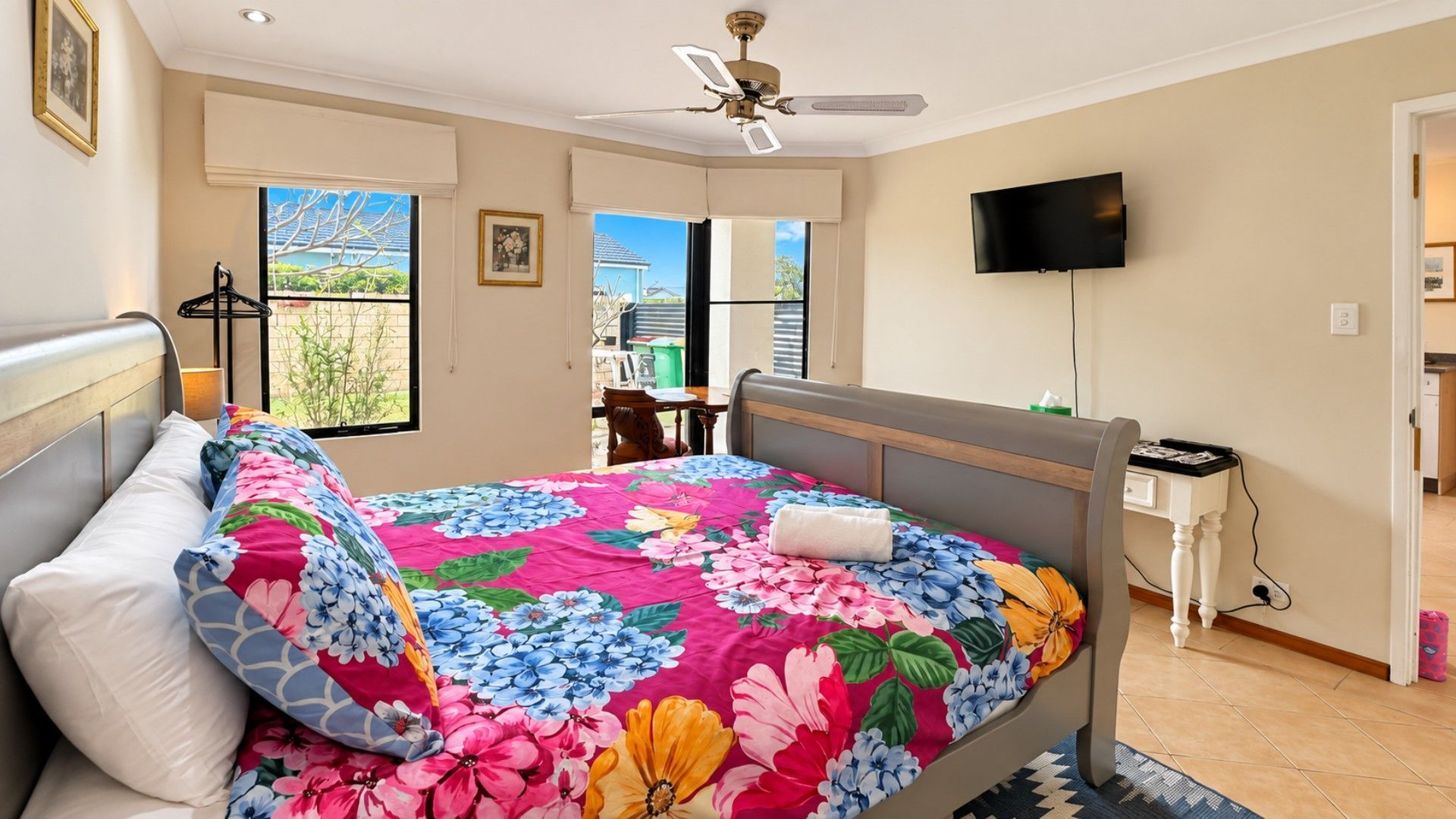 A bedroom with a bed, a ceiling fan, a TV, and a window with a view.
