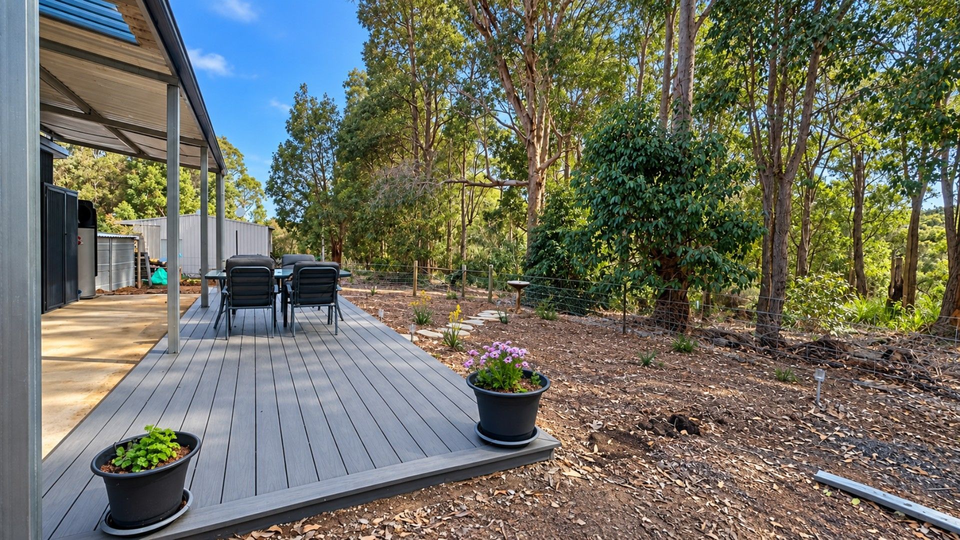 A deck with outdoor furniture, surrounded by a garden with trees and plants.