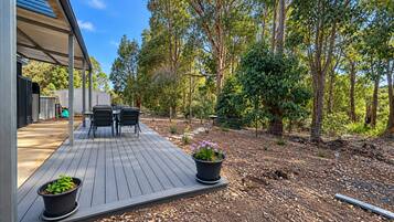 A deck with outdoor furniture, surrounded by a garden with trees and plants.