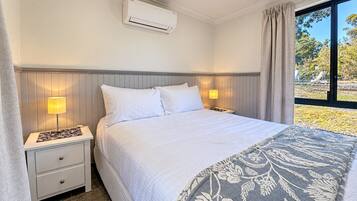 Ein Hotelzimmer mit Bett, Nachttischlampen, einem Fenster mit Vorhängen und einer Klimaanlage.