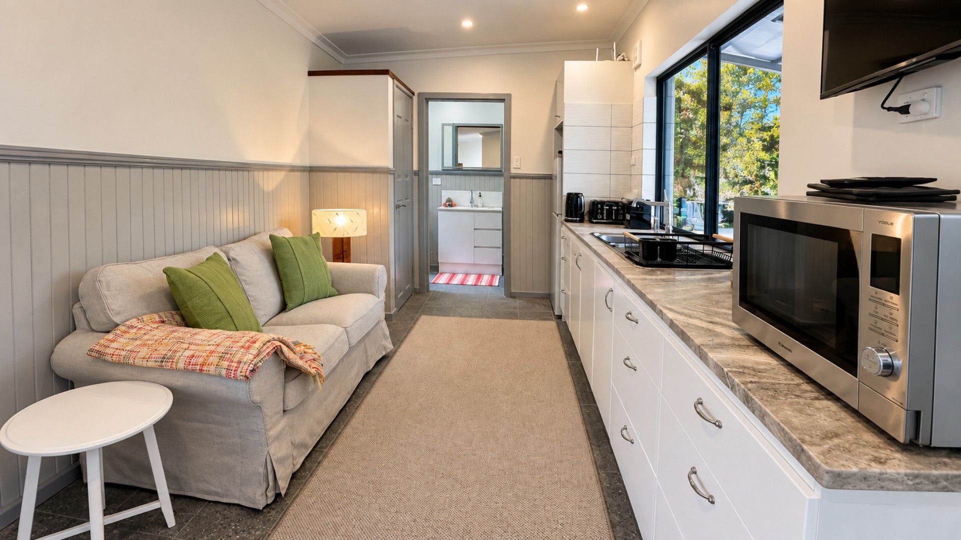 Eine kompakte Küche mit integriertem Mikrowellenherd, ein Essbereich mit Sofa und kleinem Tisch sowie ein Blick durch ein Fenster.