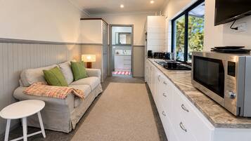 Eine kompakte Küche mit integriertem Mikrowellenherd, ein Essbereich mit Sofa und kleinem Tisch sowie ein Blick durch ein Fenster.