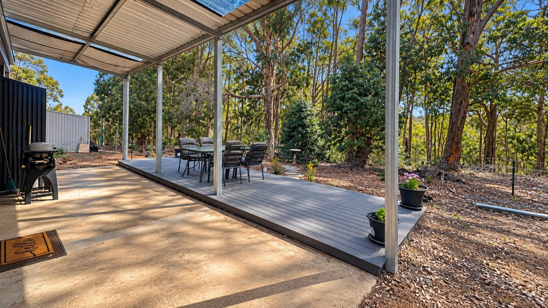 An outdoor patio area with a wooden deck, metal pergola, and a seating arrangement.