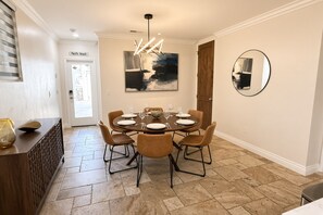 A dining area with a round table, six chairs, and a modern chandelier. - Pacific Beach: Private Backyard, BBQ, Garage, AC (San Diego)