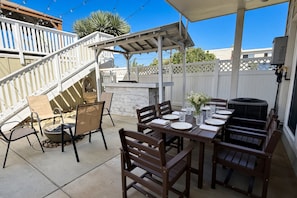 Un patio al aire libre con una mesa de comedor preparada para cuatro personas, rodeado de sillas de madera y un hogar de piedra.
