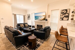 A modern living room with a fireplace, leather sofas, a coffee table, and a bar area. - Pacific Beach: Private Backyard, BBQ, Garage, AC (San Diego)