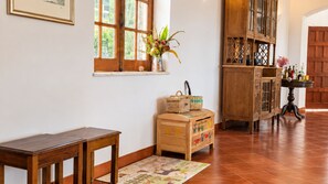 Ein Holzkabinett mit Glastüren, ein kleiner Tisch, ein Korbwäscher und ein farbenfroher Teppich auf Fliesenboden.