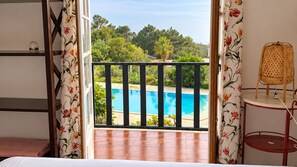 Une chambre avec vue sur une piscine, un balcon doté d’une balustrade et un fauteuil en osier.