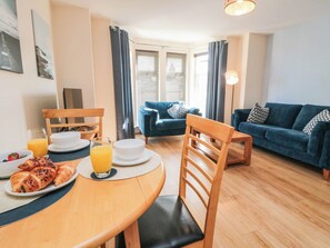A dining area with a table set for breakfast, including croissants and a glass of orange juice. There is a blue sofa and a wooden chair in the background. - Apartment 17, St. John's (Whitby)