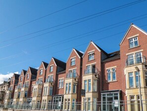 A row of red brick townhouses with multiple stories, each featuring a balcony and a bay window. - Apartment 17, St. John's (Whitby)