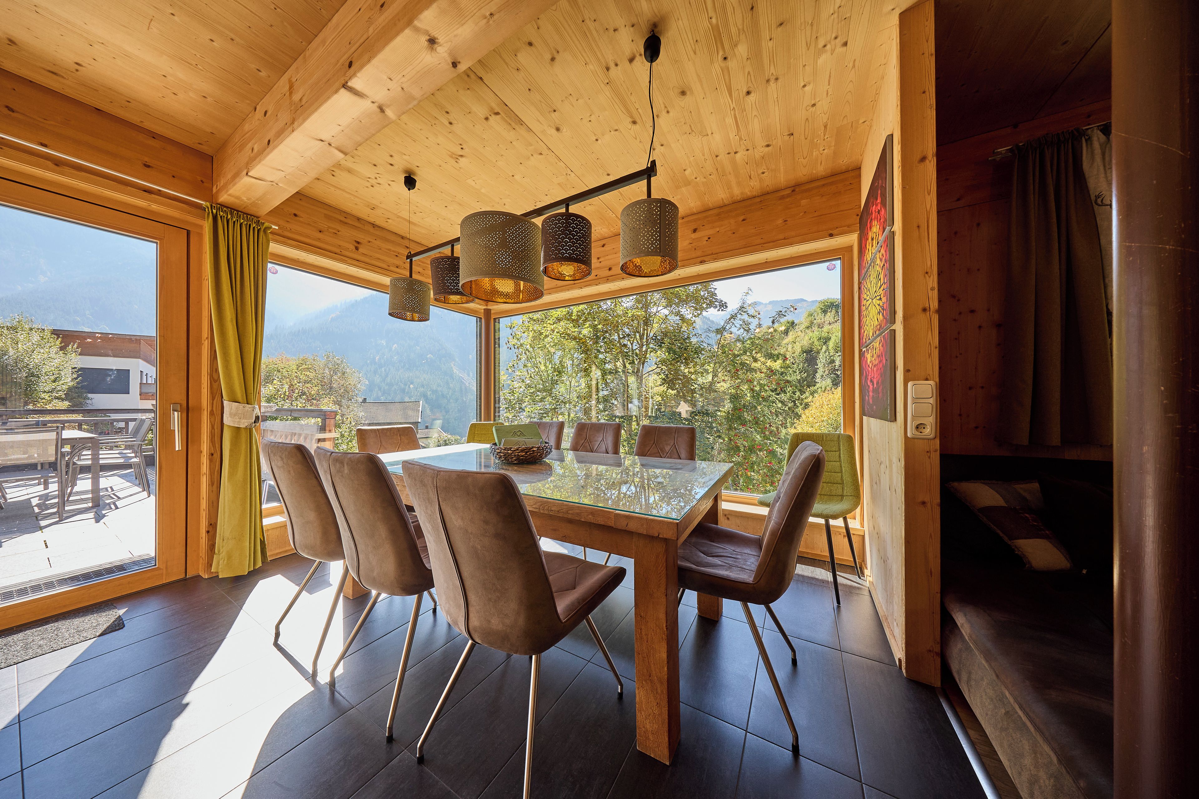 A wooden interior with a dining table, chairs, and a view of mountains.