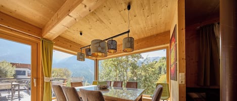 A wooden interior with a dining table, chairs, and a view of mountains.