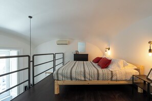 Ein Schlafzimmer mit Bett, Nachttisch, Lampe und Blick ins Freie.
