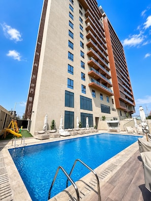 A modern hotel with a swimming pool, outdoor seating, and a children's play area. - Harmonia 1118 (Accra)