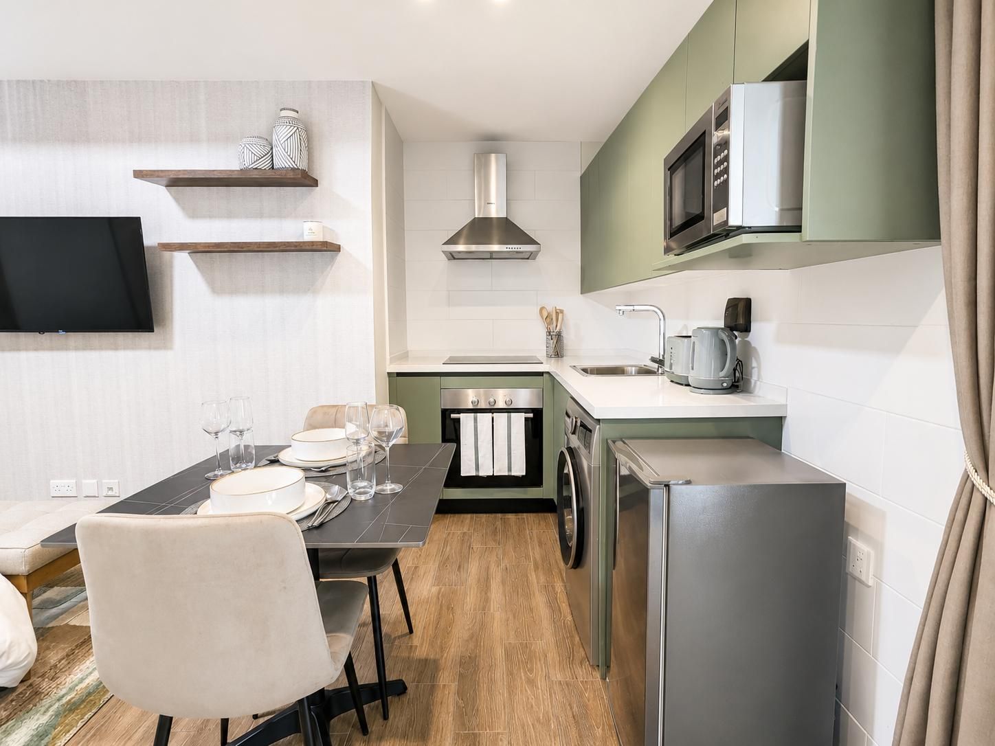 A compact kitchen with a microwave, oven, and sink. There is a dining table with chairs and a television mounted on the wall.