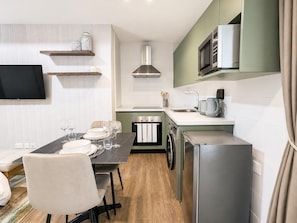 A compact kitchen with a microwave, oven, and sink. There is a dining table with chairs and a television mounted on the wall. - Harmonia 1118 (Accra)
