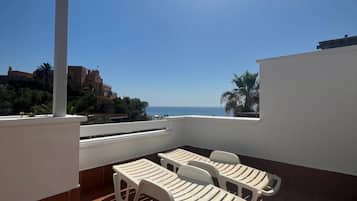 Una terraza con vista al mar, que incluye una pérgola, sillas de plástico blanco y una mesa.