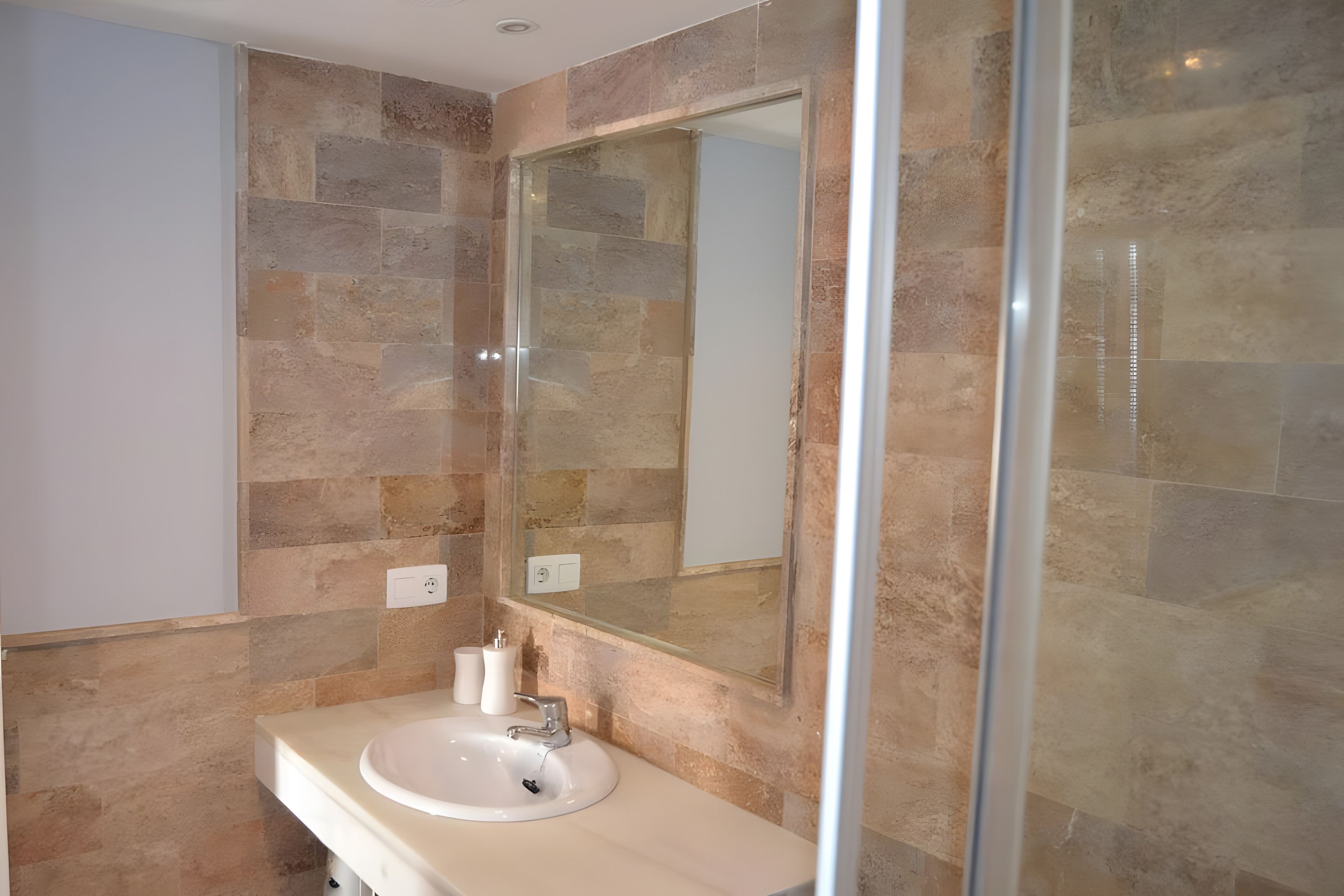 A bathroom with a white sink, a mirror, and stone tiles.