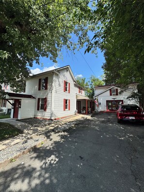 A residential area with a two-story house featuring a porch and a red car parked in front.