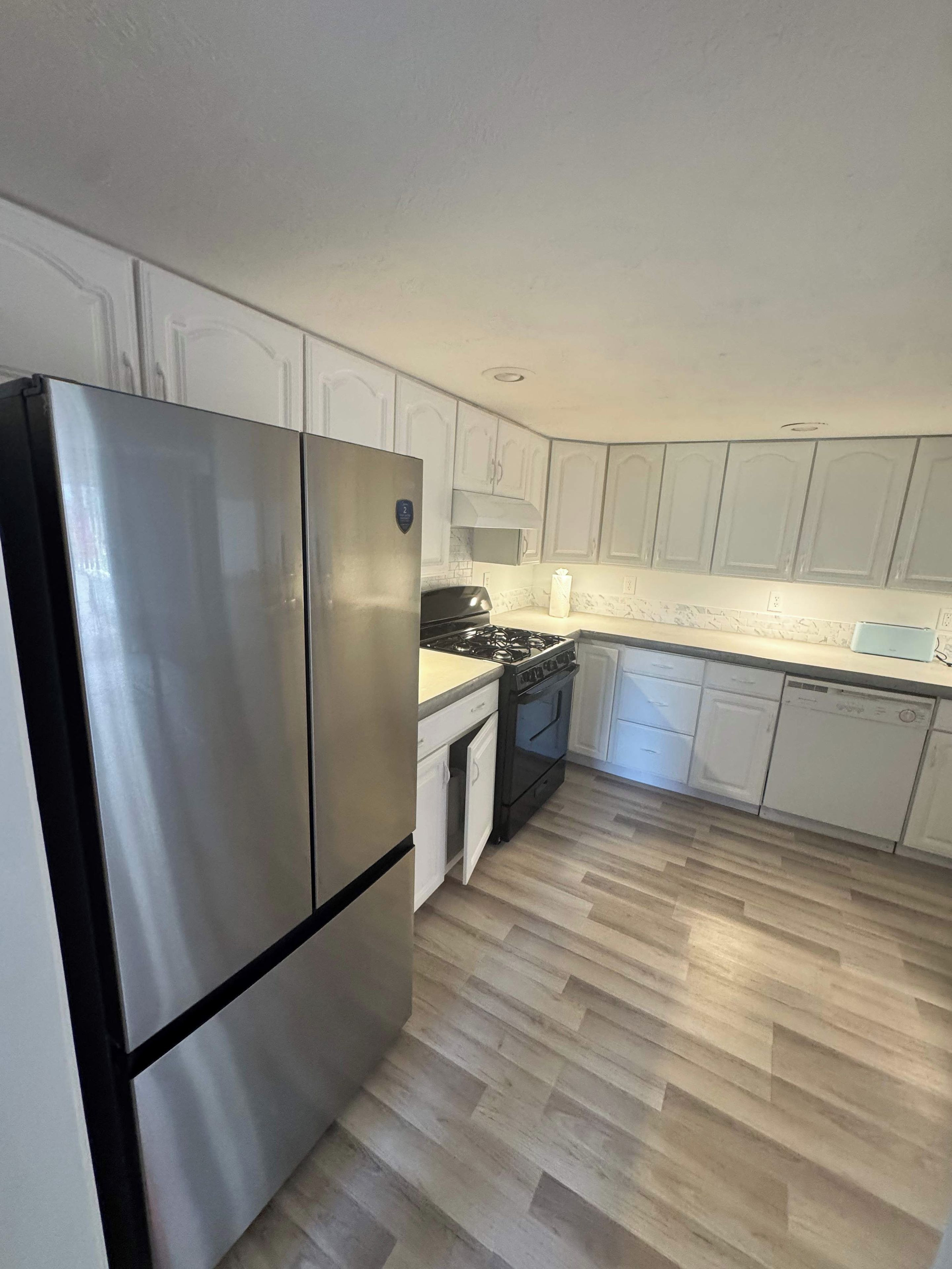 A kitchen with white cabinets, a stainless steel refrigerator, a stove, and a dishwasher.