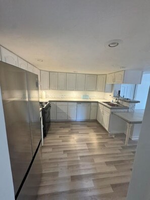 A kitchen with white cabinets, a stainless steel refrigerator, and a wooden floor. - The Grateful Trail House-Garcia A 2-bdrm apartment in Mountain Cumberland, MD. (Cumberland)