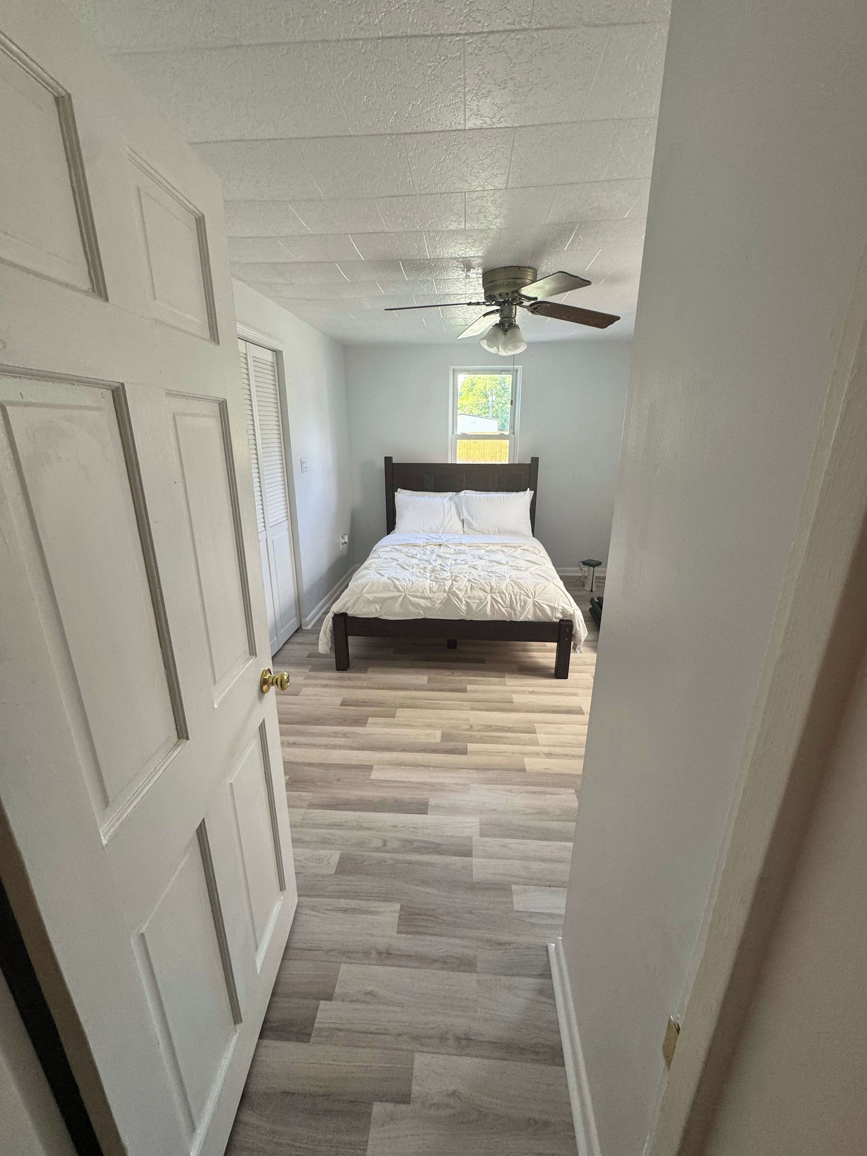Ein Schlafzimmer mit Bett, Deckenventilator, Fenster und Tür.