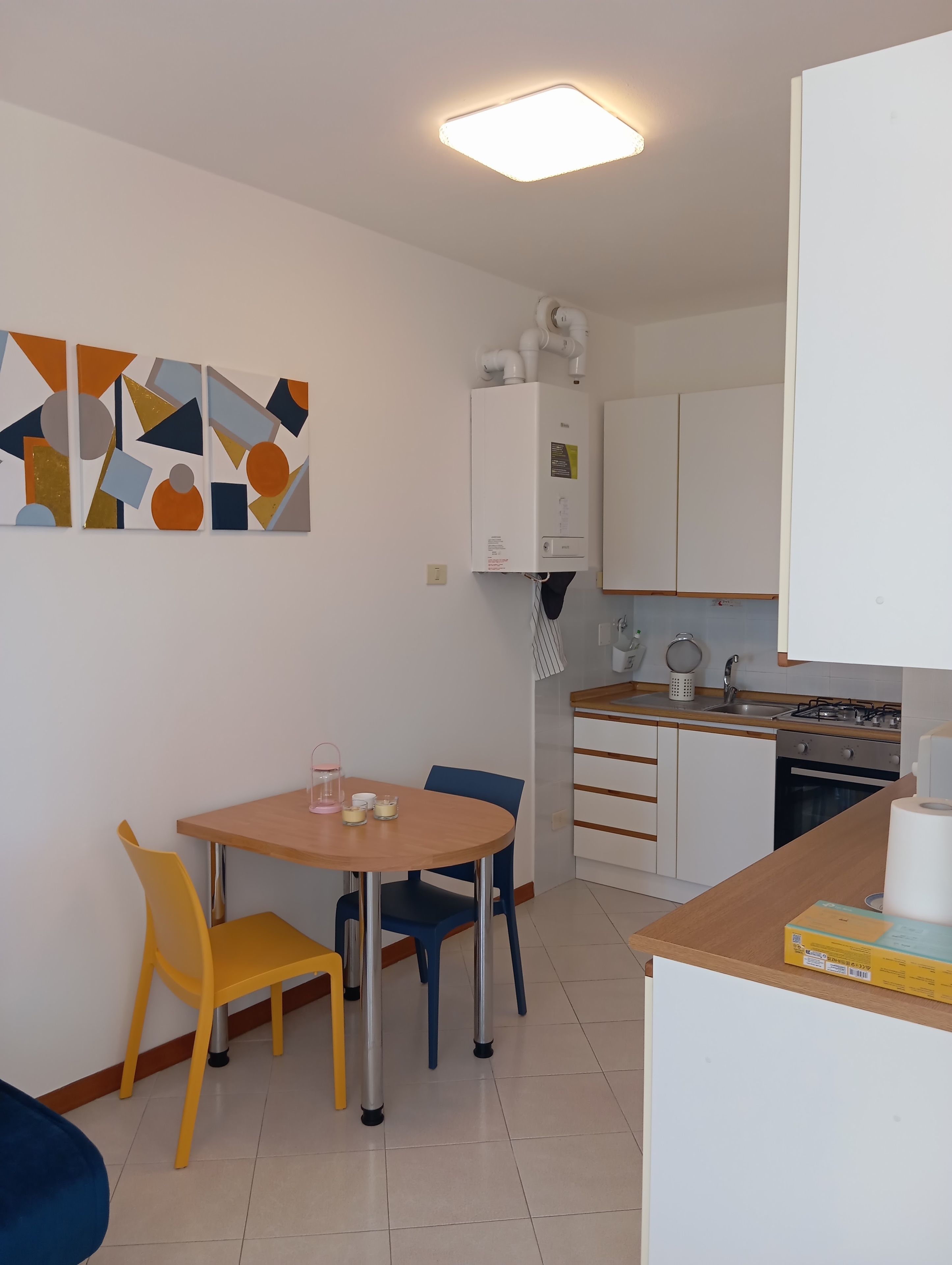 A compact kitchen with a dining area, a water heater, and a modern abstract art piece on the wall.