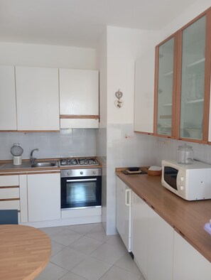 Een keuken met witte kastjes, een fornuis, oven, magnetron en een houten aanrecht.