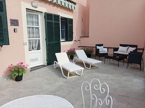 Eine Terrasse mit zwei weißen Liegestühlen, einem kleinen runden Tisch und einem dekorativen Metallgegenstand.