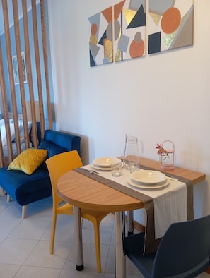 A dining area with a table set for two, a blue sofa, and abstract wall art. - "Cammaryhouse" independent apartment, panoramic terrace, private parking, AC & Wi-Fi (Casarza Ligure)