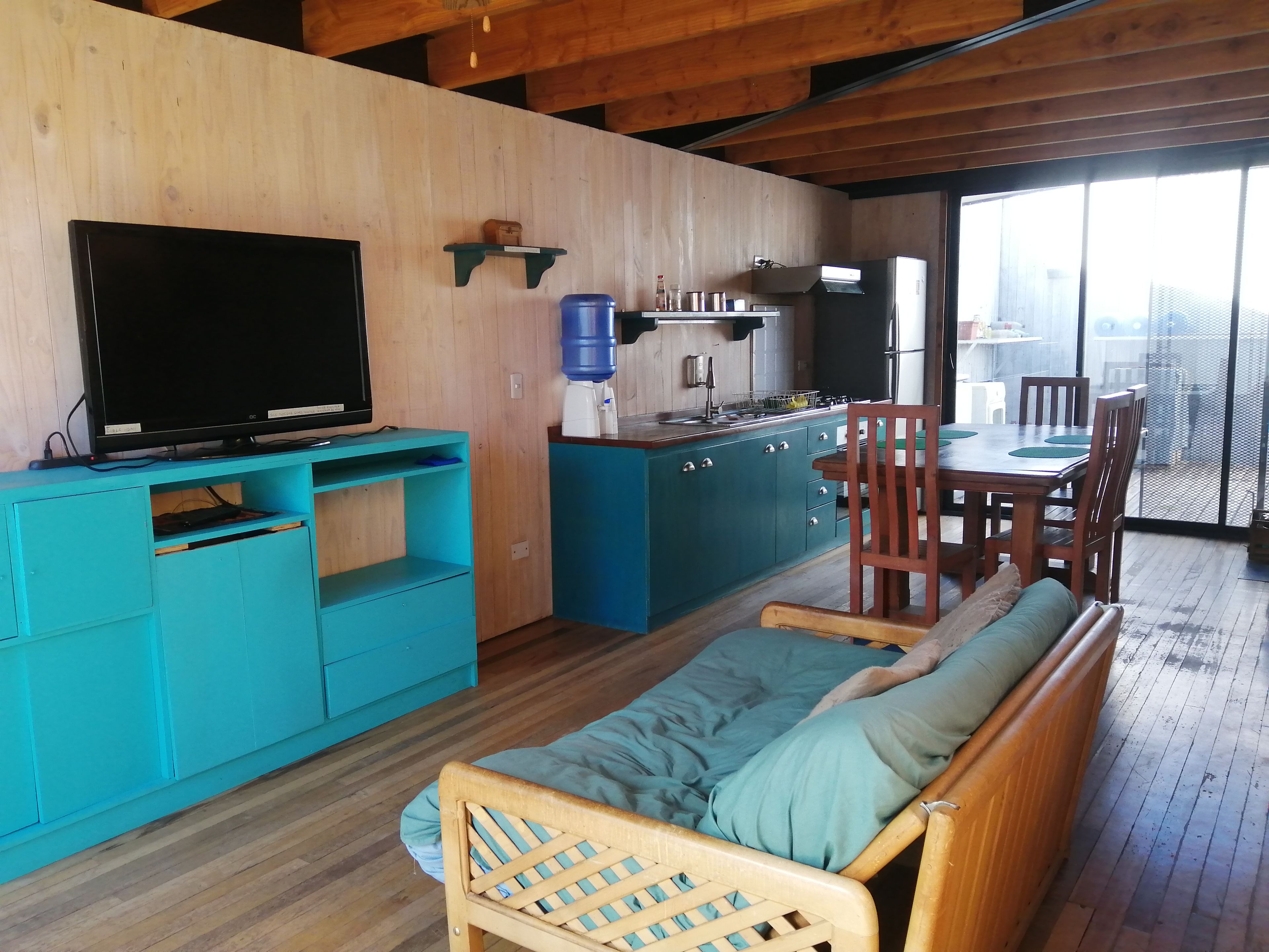 A cozy living space with a sofa, a television, a kitchen area, and a dining table with chairs.