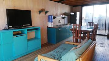 A cozy living space with a sofa, a television, a kitchen area, and a dining table with chairs.