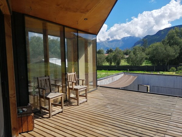 Una terraza de madera con sillas y una mesa, con vista a un paisaje montañoso.