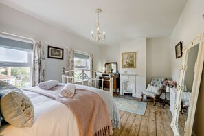 Quarto com uma cama grande, um candelabro, cômoda, espelho e vista para o exterior.