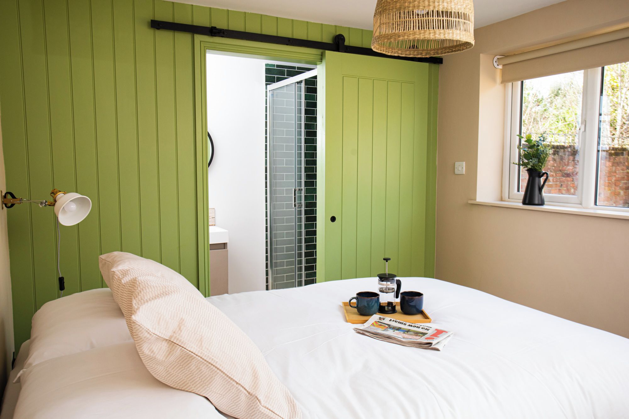 Ein Schlafzimmer mit Bett, Nachttischlampe, Fenster mit Blick und einer Tür zum Badezimmer.