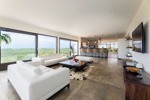 Un vaste espace de vie agrémenté d’un canapé blanc moderne, d’une table basse et d’une grande fenêtre donnant sur un paysage verdoyant.