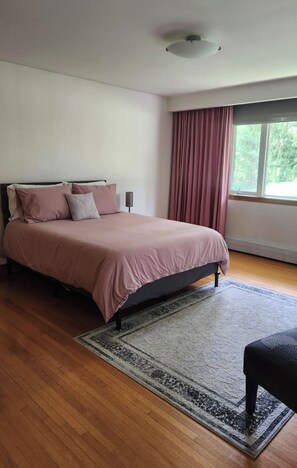 A bedroom with a bed, a rug, a window with curtains, and a ceiling light.