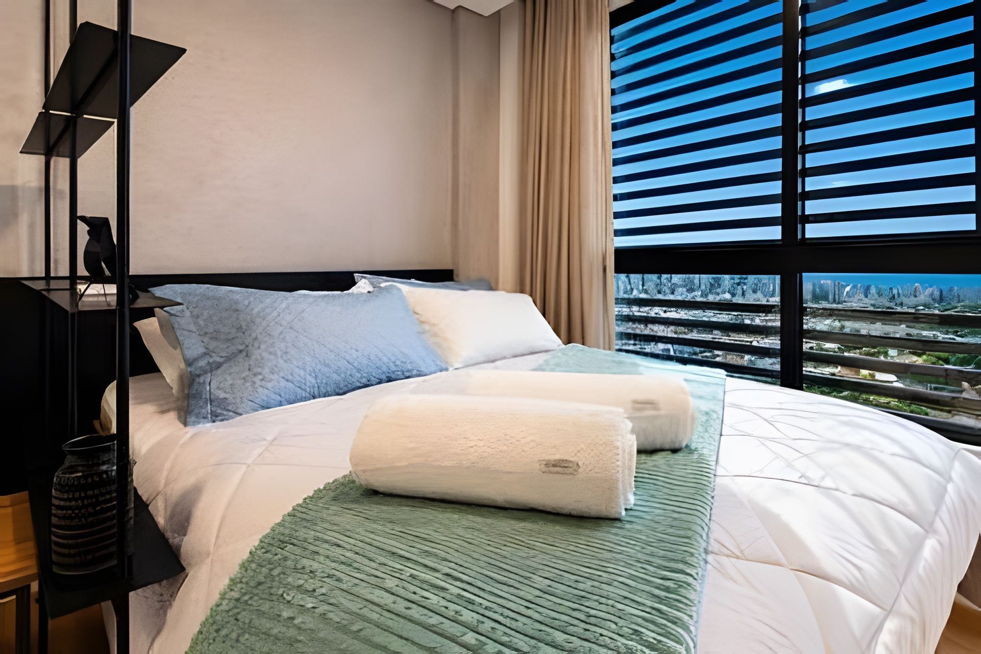 Ein modernes Hotelzimmer mit einem großen Bett, Blick auf die Stadt durch raumhohe Fenster und einer minimalistischen Einrichtung.
