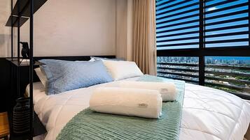 Ein modernes Hotelzimmer mit einem großen Bett, Blick auf die Stadt durch raumhohe Fenster und einer minimalistischen Einrichtung.