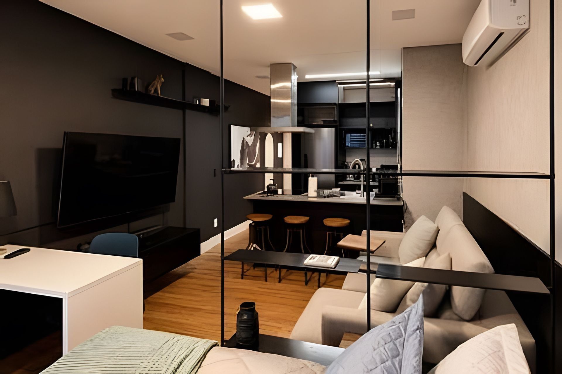 Una sala moderna con un sofá, una mesa de centro y un televisor. Hay una zona de cocina con una barra y taburetes.